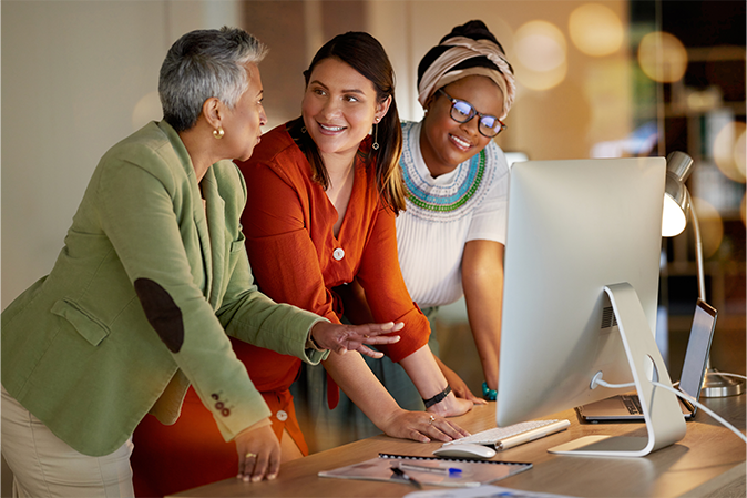 Three women talking in front of a computer screen