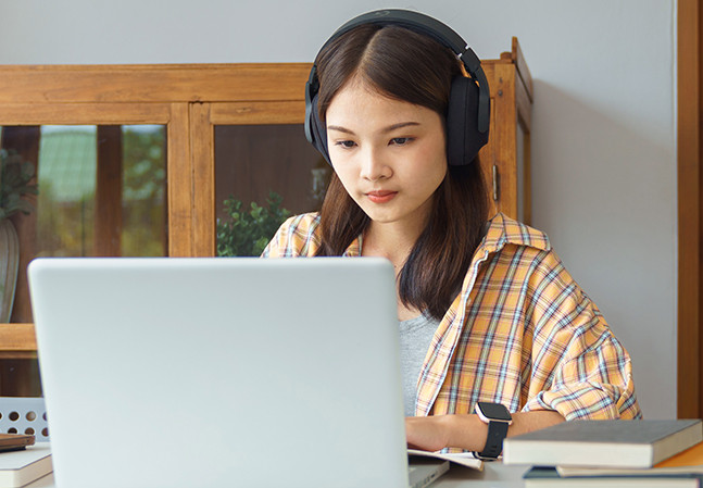 young woman studying at desk with laptops, books and headphone